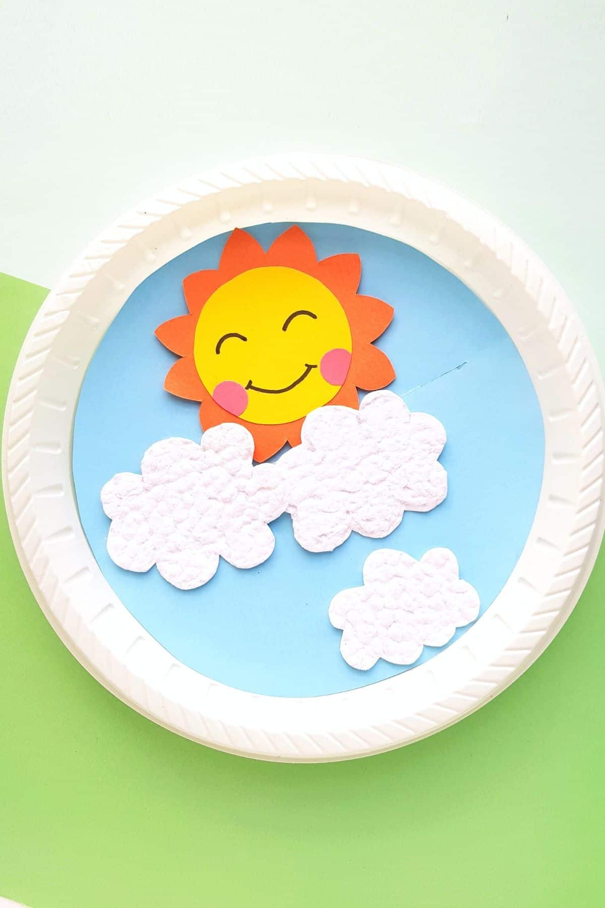 Smiling paper sun above white clouds on a blue paper plate